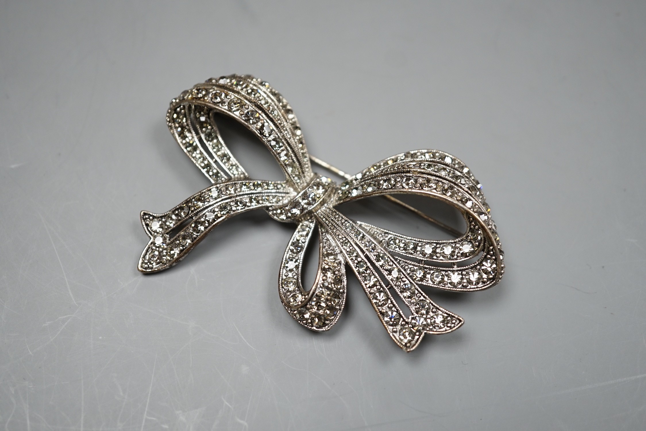 A white metal and paste set ribbon bow brooch, 77mm.